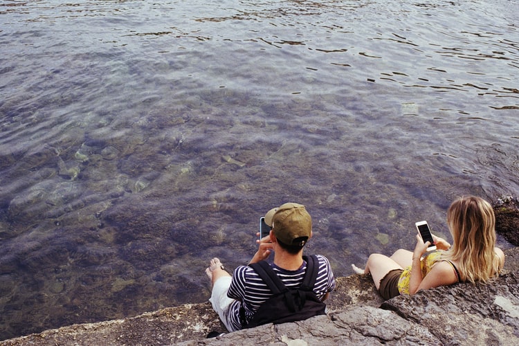 deux adolescents distraits par leur téléphone au lieu de communiquer ou de regarder la mer, devant eux : une allégorie du TDAH
